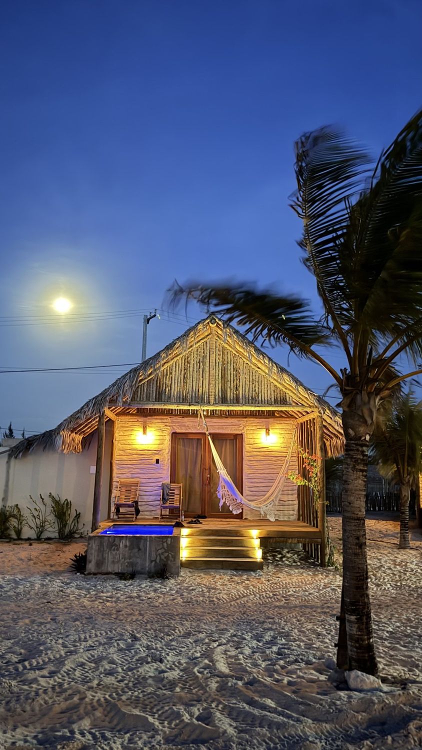 Chalé da Pousada Aruê iluminado à noite, com lua cheia e coqueiro