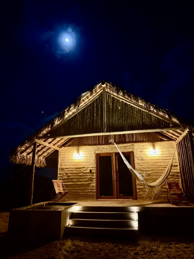 Bangalô iluminado sob a lua cheia, com rede na varanda