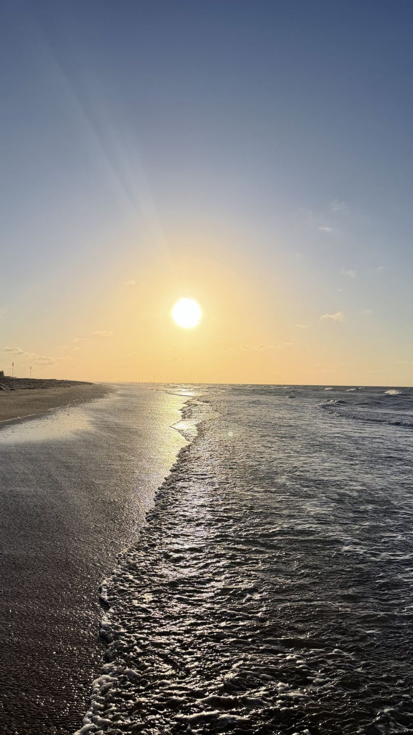 Sol baixo sobre o mar e a areia molhada