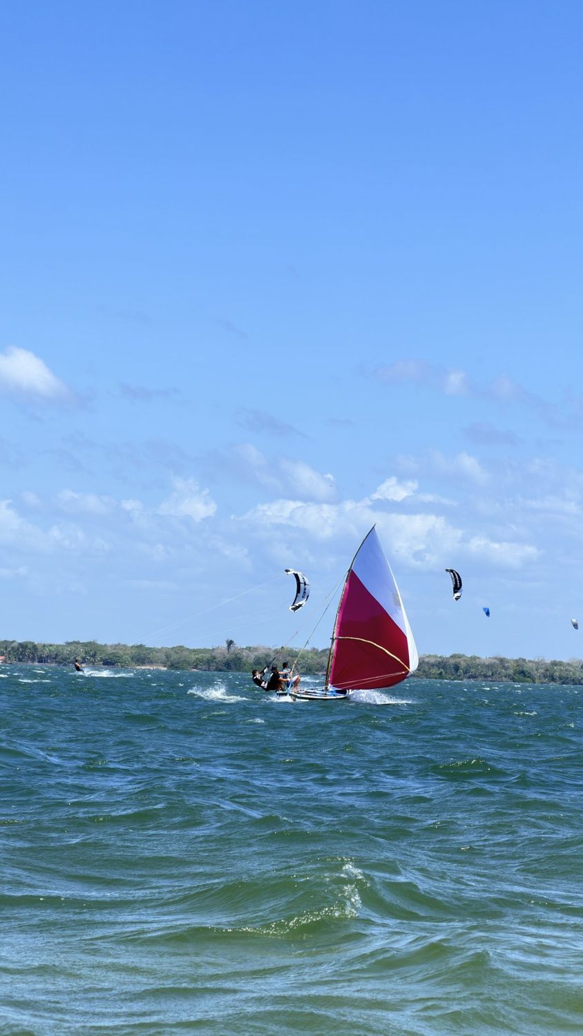 Barco a vela vermelho e kites sobre o mar verde de Tatajuba